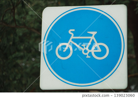 Blue bicycle lane sign with white bike symbol installed outdoors, traffic regulation symbol indicating designated cycling route. Blue bicycle lane sign with white bike symbol installed outdoors, traffic regulation symbol indicating designated cycling route. 139023060