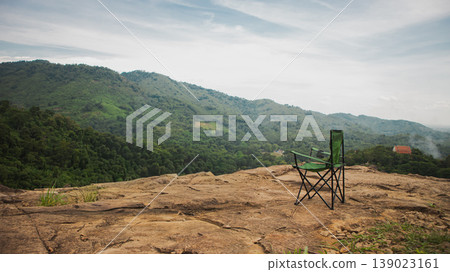 Camping chair on rocky mountain viewpoint overlooking green hills and forest valley. Scenic outdoor travel scene symbolizing freedom, adventure, relaxation and peaceful nature escape. 139023161