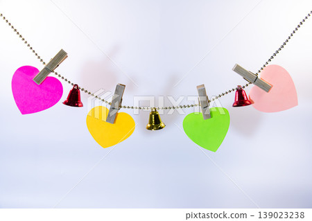 Colorful heart shaped paper notes hanging on string with small bells and clothespins isolated on white background. Romantic decoration template with copy space for love message. Colorful heart shaped paper notes hanging on string with small bells and clothespins isolated on white background. Romantic decoration template with copy space for love message. 139023238