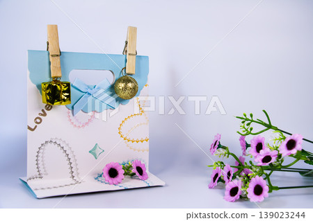 Decorative gift bag with ribbon, golden ornaments and pink flowers isolated on white background. Still life concept for celebration, love, holiday decoration and gift packaging. Decorative gift bag with ribbon, golden ornaments and pink flowers isolated on white background. Still life concept for celebration, love, holiday decoration and gift packaging. 139023244
