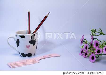 Pencils in ceramic cup with pink comb and small flowers on white background. Minimal study and lifestyle still life concept with copy space. 139023250