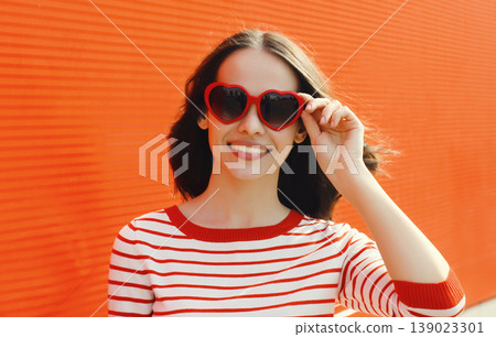 Beautiful happy young woman posing in red heart shaped sunglasses Beautiful happy young woman posing in red heart shaped sunglasses 139023301