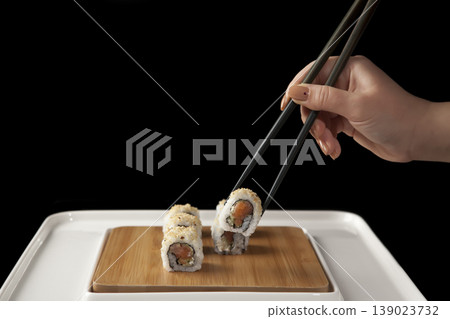 Hand Taking Sushi with Chopsticks. Japanese Cuisine Sushi Being Picked with Chopsticks. 139023732