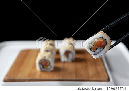 Hand Taking Sushi with Chopsticks. Japanese Cuisine Sushi Being Picked with Chopsticks. 139023734