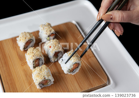 Hand Taking Sushi with Chopsticks. Japanese Cuisine Sushi Being Picked with Chopsticks. 139023736