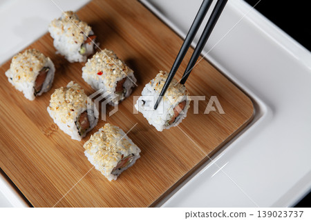 Hand Taking Sushi with Chopsticks. Japanese Cuisine Sushi Being Picked with Chopsticks. 139023737