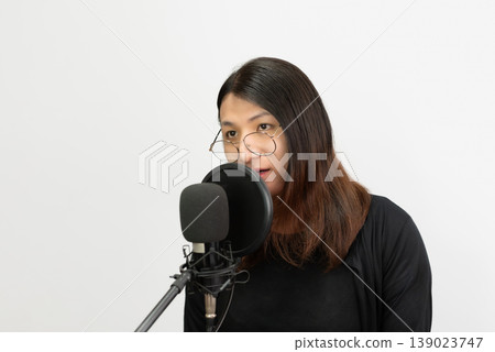 Young lgbtq woman wearing glasses speaking into microphone in studio isolated background content creator communication podcast audio recording modern lifestyle technology Young lgbtq woman wearing glasses speaking into microphone in studio isolated background content creator communication podcast audio recording modern lifestyle technology 139023747