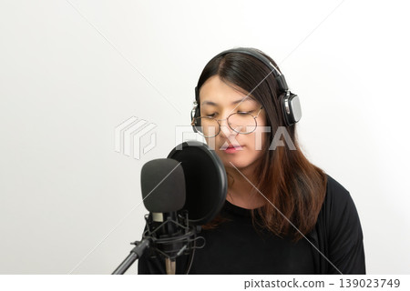 Young lgbtq woman wearing headphones speaking into microphone in studio isolated background podcast recording audio production communication modern lifestyle technology content creator Young lgbtq woman wearing headphones speaking into microphone in studio isolated background podcast recording audio production communication modern lifestyle technology content creator 139023749