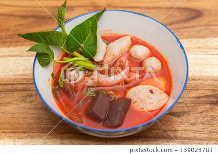 Yentafo Thai pink noodle soup with seafood fish balls blood tofu and morning glory in rich red broth served in bowl on wooden table Yentafo Thai pink noodle soup with seafood fish balls blood tofu and morning glory in rich red broth served in bowl on wooden table 139023781