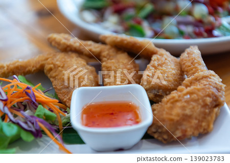 Crispy fried chicken wings served with sweet chili sauce and fresh salad on plate showing crunchy texture and delicious appetizer style on wooden table Crispy fried chicken wings served with sweet chili sauce and fresh salad on plate showing crunchy texture and delicious appetizer style on wooden table 139023783