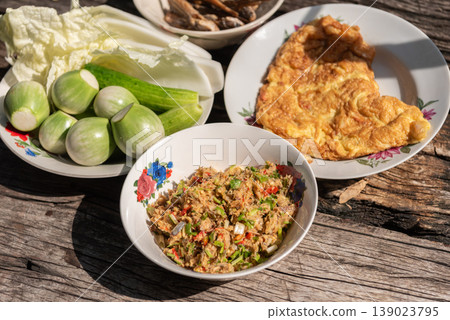 Traditional Thai meal with spicy dip fresh vegetables and omelet served on rustic wooden table authentic local cuisine healthy and flavorful food concept Traditional Thai meal with spicy dip fresh vegetables and omelet served on rustic wooden table authentic local cuisine healthy and flavorful food concept 139023795