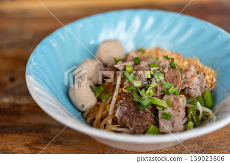 Delicious Thai dry noodles with sliced pork meatballs bean sprouts and green onions served in bowl on wooden table with rich flavor and street food style Delicious Thai dry noodles with sliced pork meatballs bean sprouts and green onions served in bowl on wooden table with rich flavor and street food style 139023806