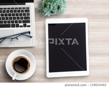 Top view blank tablet,glasses,notebook and cup of coffee on wood table background. Top view blank tablet,glasses,notebook and cup of coffee on wood table background. 139024483