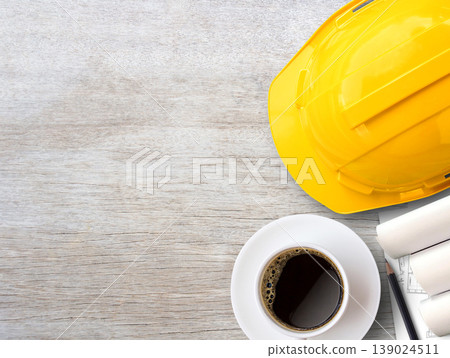 Yellow safety helmet or hard hat and construction paper plans on wood table background. Yellow safety helmet or hard hat and construction paper plans on wood table background. 139024511