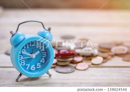 Coins and blue alram clock on wood table background. Coins and blue alram clock on wood table background. 139024548