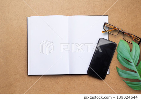Top view with blank notebook,smartphone,glasses,green leave on brown wood table background. Top view with blank notebook,smartphone,glasses,green leave on brown wood table background. 139024644