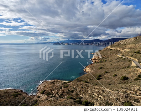 Aerial Coastal Cliff Overlooking Turquoise Sea And Winding Path With Dramatic Clouds And Distant City Skyline Aerial Coastal Cliff Overlooking Turquoise Sea And Winding Path With Dramatic Clouds And Distant City Skyline 139024911