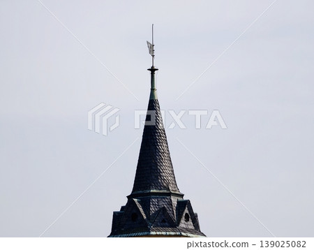 Slate Tower Cuts Through Pale Daytime Sky. Weathered Roof With Sleek Geometric Design And Airy Backdrop Slate Tower Cuts Through Pale Daytime Sky. Weathered Roof With Sleek Geometric Design And Airy Backdrop 139025082