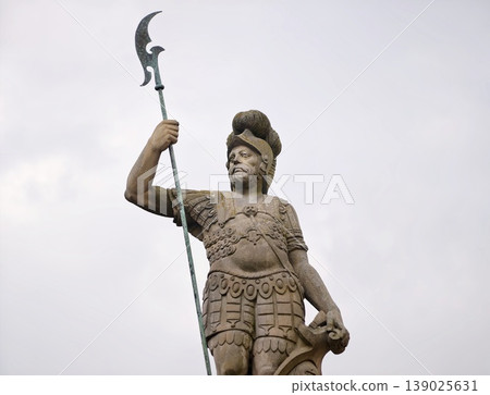 Imposing Stone Figure Of Soldier With Spear Overlooking Cityscape For Heritage Recognition Imposing Stone Figure Of Soldier With Spear Overlooking Cityscape For Heritage Recognition 139025631