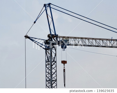 Modern Crane Under Cloudy Sky Viewed. Construction Site With Crane Silhouetted Against Gray Sky Modern Crane Under Cloudy Sky Viewed. Construction Site With Crane Silhouetted Against Gray Sky 139025635