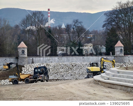 Heavy Machinery In Mountain Construction. Village Skyline Under Cloudy Sky With Construction Activity Heavy Machinery In Mountain Construction. Village Skyline Under Cloudy Sky With Construction Activity 139025695