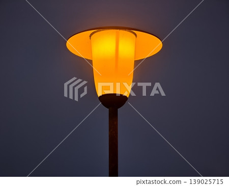 Serene Nighttime Cityscape With Lone Lamp Casting Gentle Amber Illumination Over Peaceful Walkways 139025715