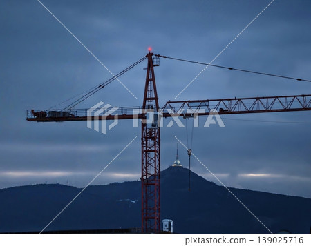 Evening Industrial Construction Scene. Silhouette Of Crane Against Evening Mountain Background 139025716