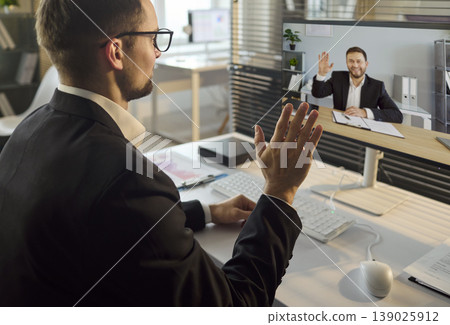 Businessman greeting male colleague on online video call in modern office Businessman greeting male colleague on online video call in modern office 139025912