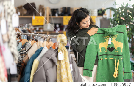Latin girl is busy looking at clothes items in store, choose sweater Latin girl is busy looking at clothes items in store, choose sweater 139025997