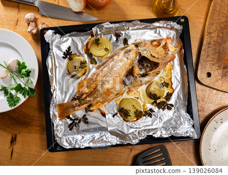 Baked red sea bream with herbs and onions on foil-wrapped tray 139026084