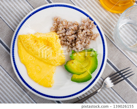 Delicious omelet with avocado and boiled buckwheat served on the tablecloth in a cafe Delicious omelet with avocado and boiled buckwheat served on the tablecloth in a cafe 139026155