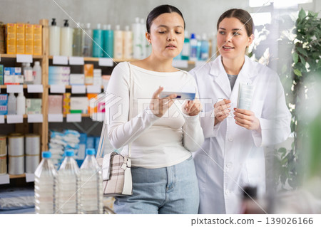 Middle-aged woman choosing ointment while pharmacist offering in drugstore Middle-aged woman choosing ointment while pharmacist offering in drugstore 139026166