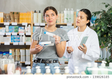 Young woman choosing ointment while pharmacist offering in drugstore Young woman choosing ointment while pharmacist offering in drugstore 139026185