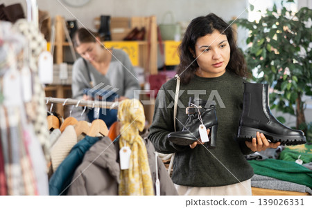 Latina female client choosing stylish boots in clothing store 139026331