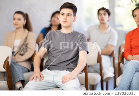 guy sits in the classroom against the background of other students and listens guy sits in the classroom against the background of other students and listens 139026335