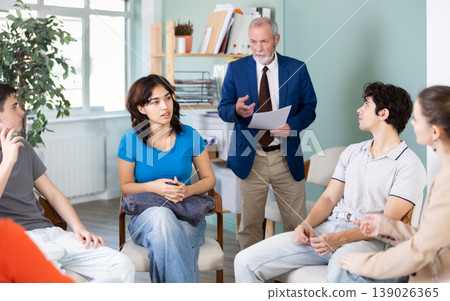 Young students sitting in circle and talking under supervision of teacher 139026365