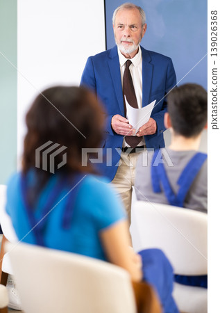 Senior teacher speaking to students in blue overalls Senior teacher speaking to students in blue overalls 139026368
