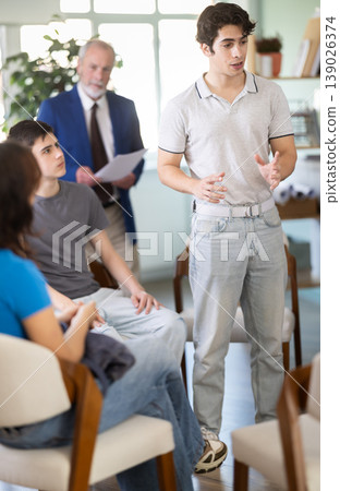 Young guy standing and talking to students sitting in a circle Young guy standing and talking to students sitting in a circle 139026374