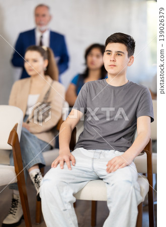 guy sits in the classroom against the background of other students and listens guy sits in the classroom against the background of other students and listens 139026379