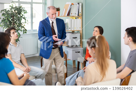 Youth girls and guys sit at circle, listen to senior man coach. Youth girls and guys sit at circle, listen to senior man coach. 139026402