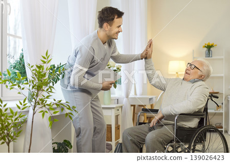 Happy caregiver giving high five to senior man in wheelchair, celebrating successful rehabilitation. Happy caregiver giving high five to senior man in wheelchair, celebrating successful rehabilitation. 139026423