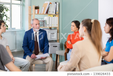 Youth girls and guys sit at circle, listen to senior man coach. 139026433