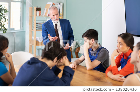 Senior manager scolding young workers sitting around table Senior manager scolding young workers sitting around table 139026436