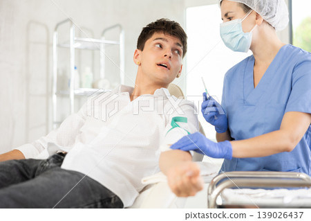 Young man having vein injection lying on clinical chair Young man having vein injection lying on clinical chair 139026437