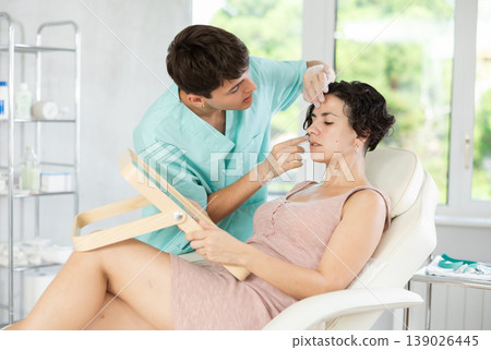 Middle-aged woman having consultation about face aesthetic while looking in the mirror 139026445