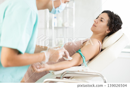 Male anesthesiologist injecting anesthetic into vein on her arm with syringe in cosmetology clinic Male anesthesiologist injecting anesthetic into vein on her arm with syringe in cosmetology clinic 139026504