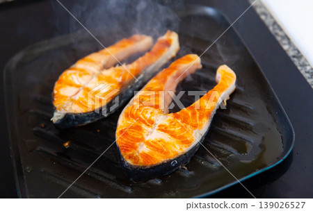 There are two pieces of broiled salmon steaks in square black frying pan 139026527