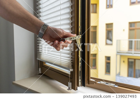 Close up of hand opening modern window handle in apartment interior with natural light Close up of hand opening modern window handle in apartment interior with natural light 139027493