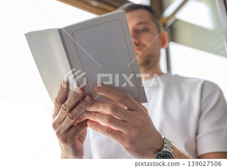 Close up of book and hands reading near window with soft daylight and shallow depth Close up of book and hands reading near window with soft daylight and shallow depth 139027506