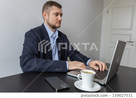 Businessman working at laptop desk with coffee and smartphone in clean modern office Businessman working at laptop desk with coffee and smartphone in clean modern office 139027531